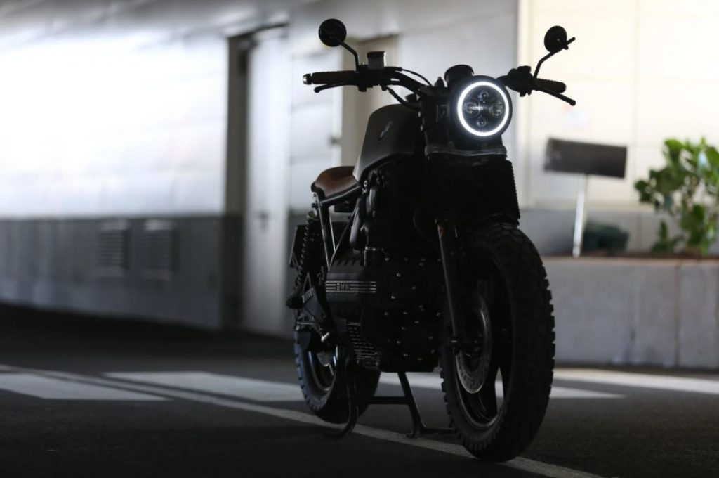 A motorcycle with its headlight illuminated, parked in a dimly lit urban environment, showcasing its sleek design