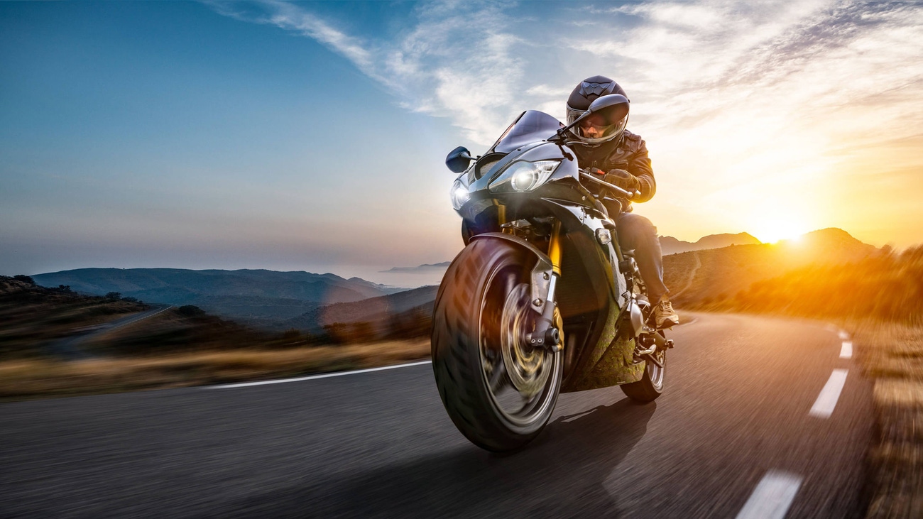 Motorcycle rider cruising a coastal road at sunset.