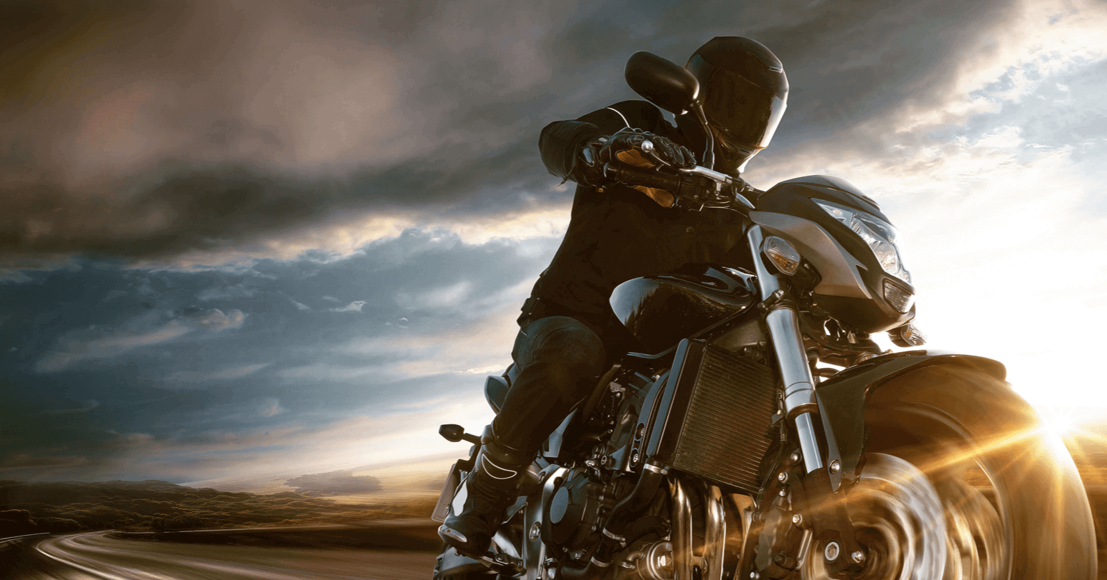 motorcyclist in black riding gear on a motorcycle with the sun setting behind