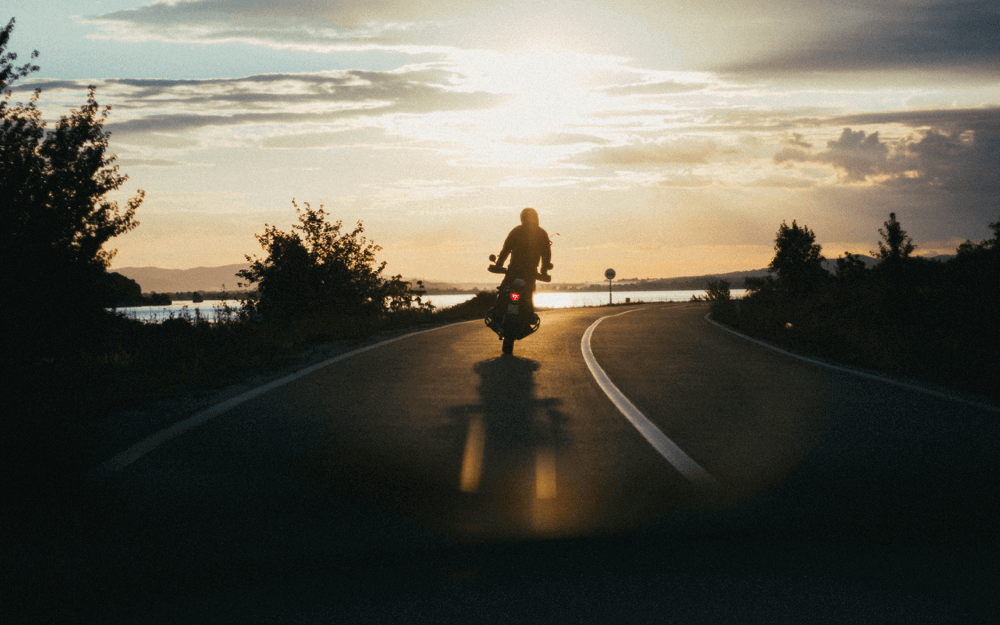 A silhouette of a motorcyclist riding on a curved road at sunset